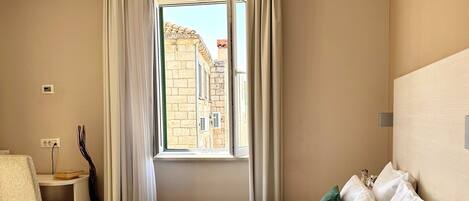 A hotel room with a bed, a chair, a small table, and a window with curtains.