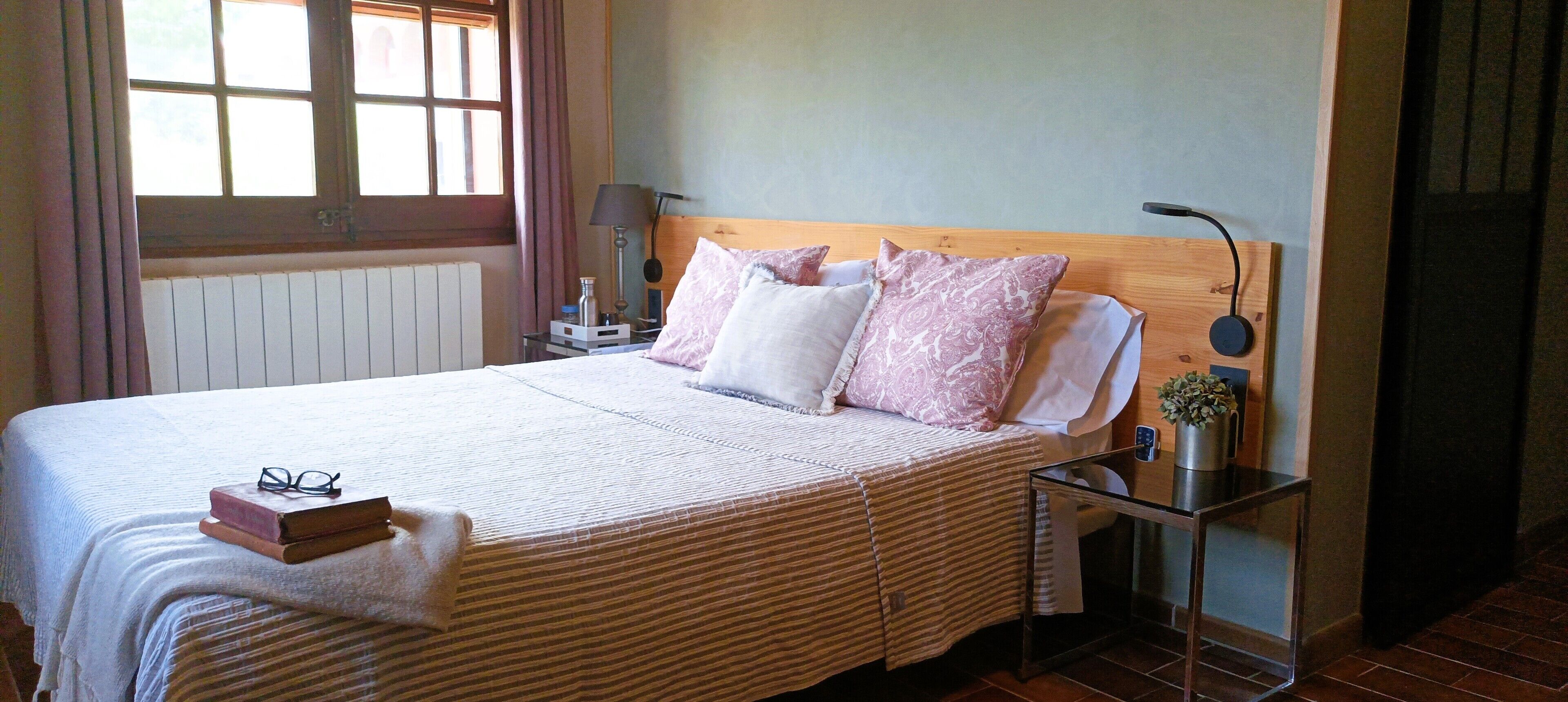Una cama bien hecha con una colcha a rayas, una mesita de noche con una lámpara y una ventana con cortinas.
