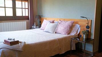 Una cama bien hecha con una colcha a rayas, una mesita de noche con una lámpara y una ventana con cortinas.