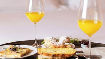 Bandeja de desayuno con diferentes platos y vasos de jugo de naranja sobre una mesa en una habitación de hotel.