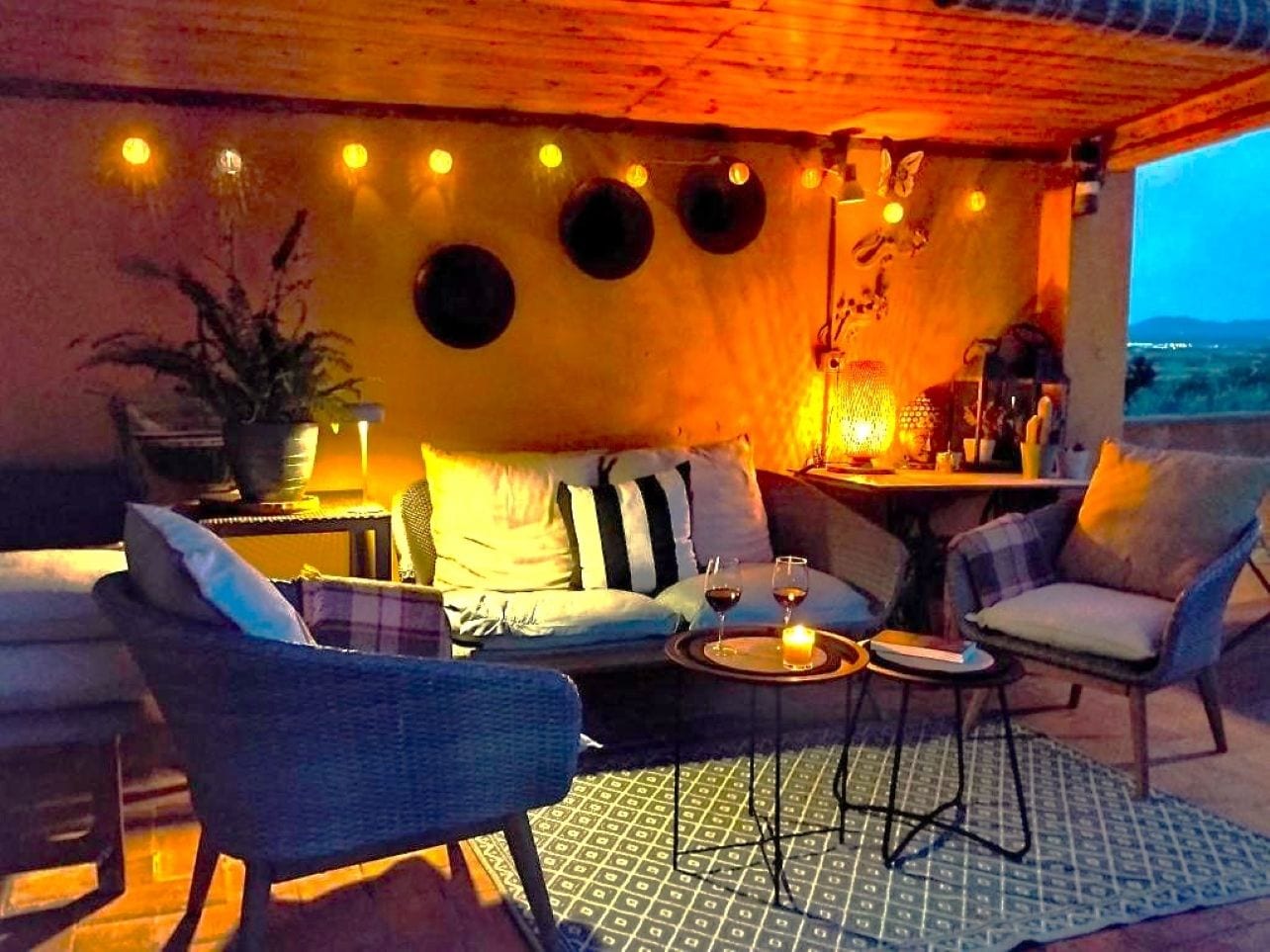 Un espacio al aire libre con sofá, sillas, una mesa y una vela.