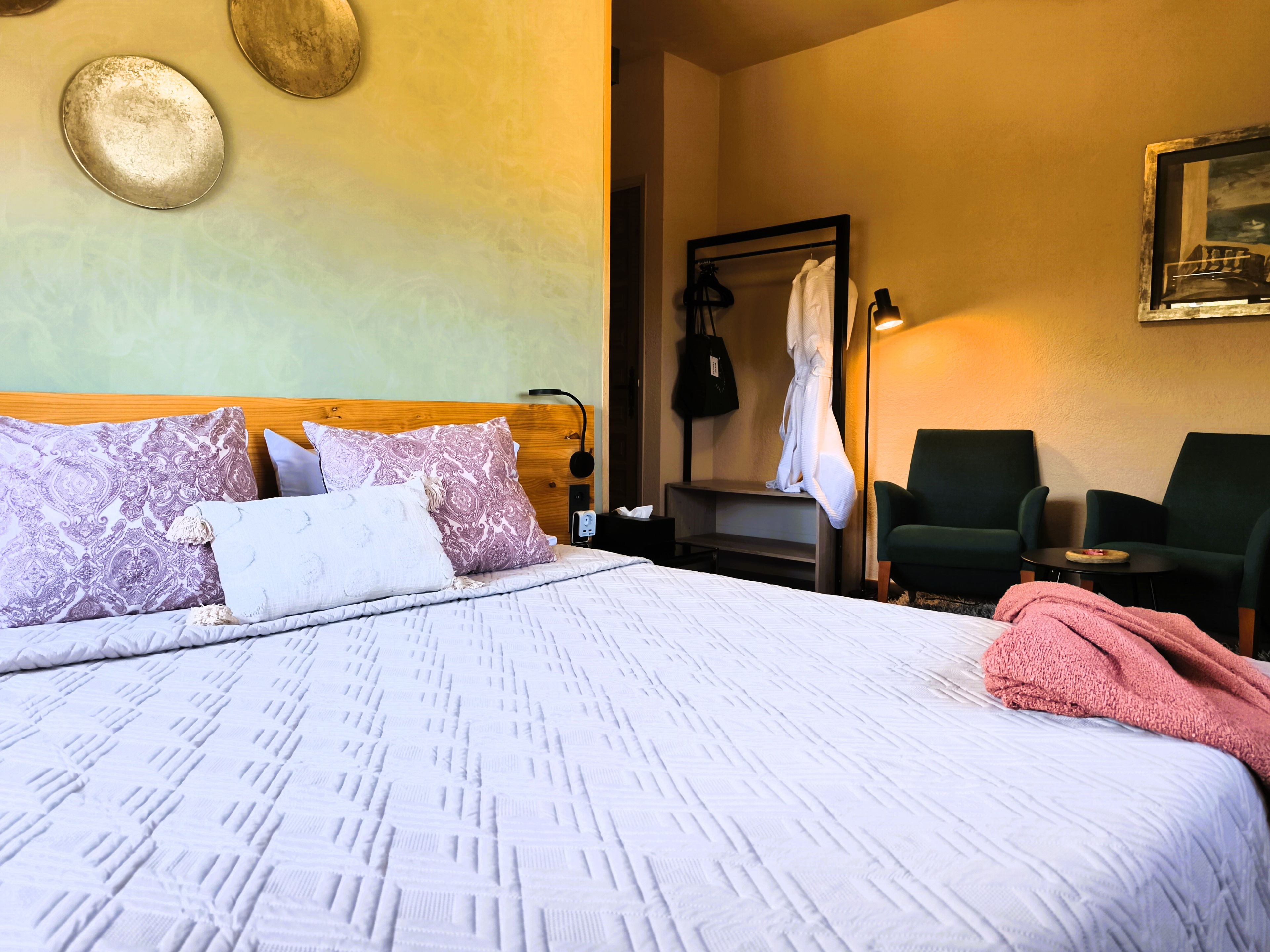 Une chambre d’hôtel comprenant un lit, une chaise, une table, un peignoir et un porte-manteau.