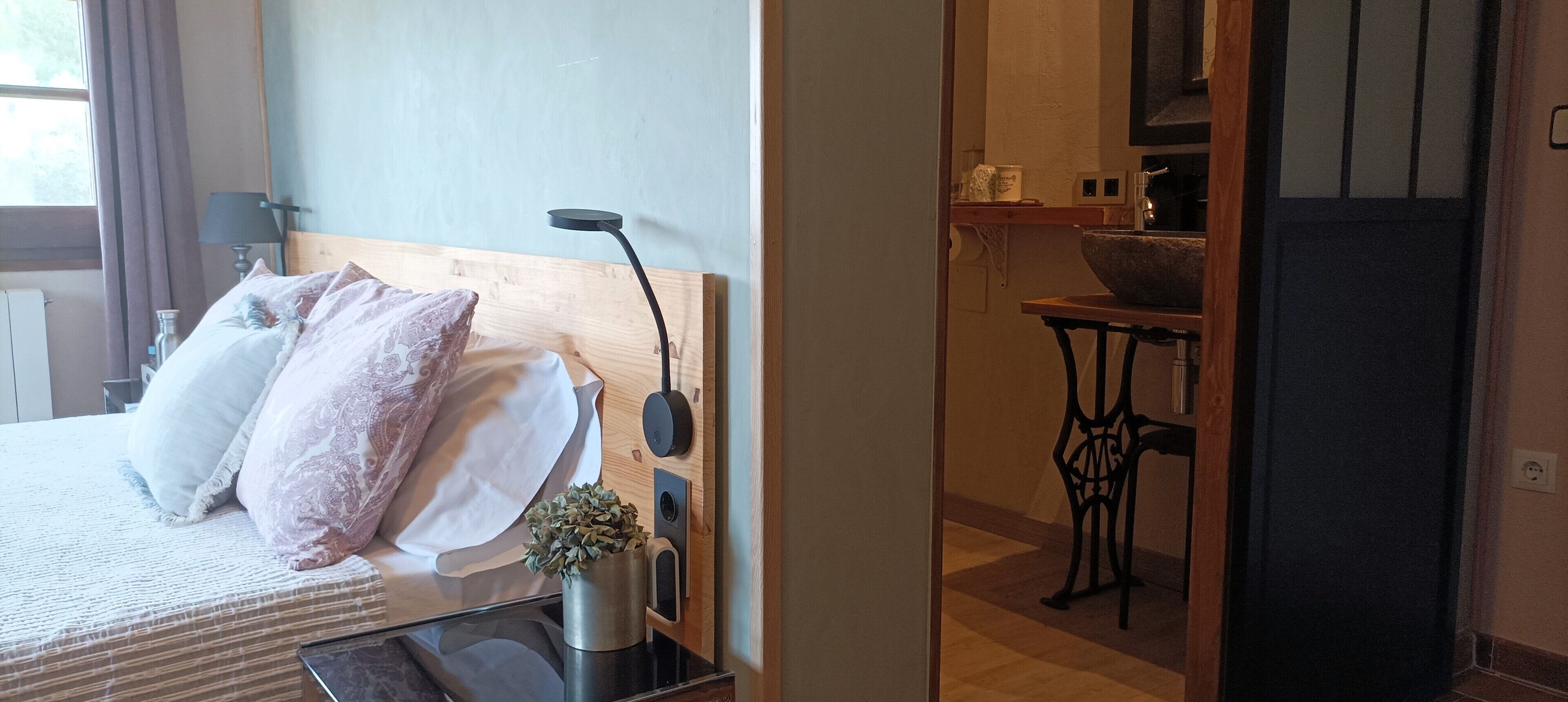 A bedroom with a bed, pillows, a bedside table with a lamp, and a small plant.