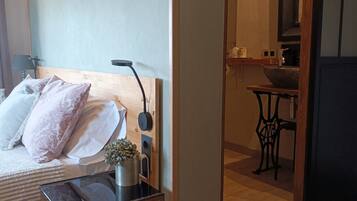 A bedroom with a bed, pillows, a bedside table with a lamp, and a small plant.