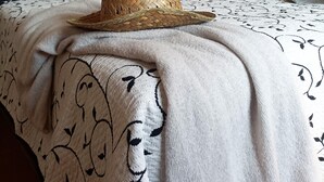 A neatly made bed with a woven hat on top, a patterned blanket, and a wall with abstract art and a hanging light fixture. - La Masia Costa Brava (Garrigas)