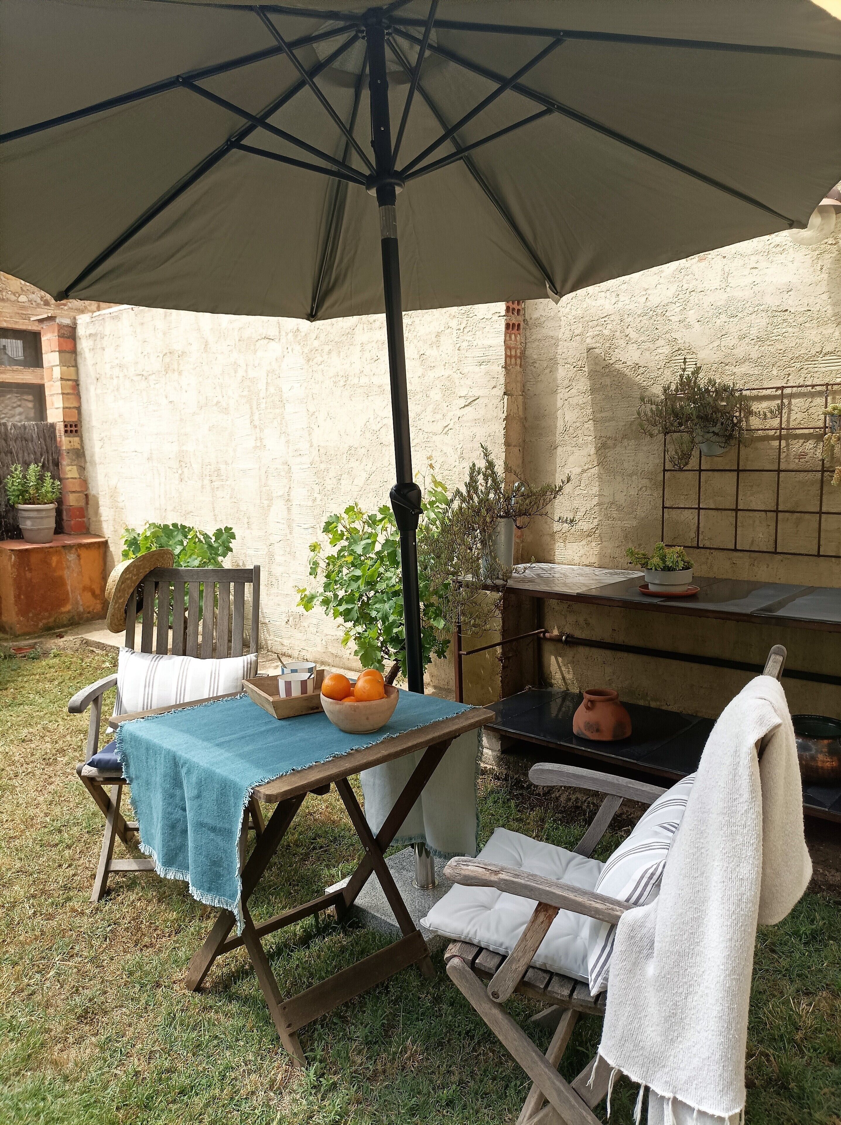 An outdoor patio with a table and chairs, a hanging plant, and a brick wall.