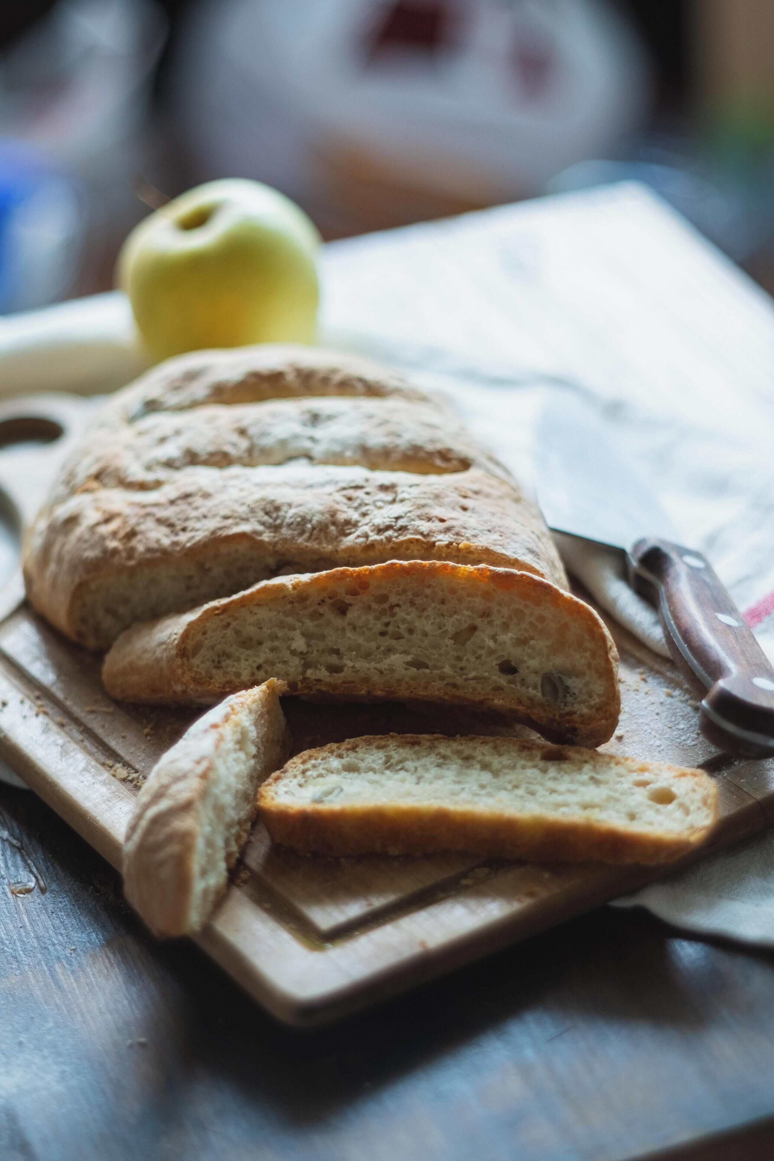 A loaf of bread on a wooden cutting board with a knife beside it.