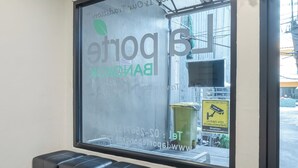 Zona de recepción con un amplio ventanal que muestra un logotipo y texto, un espacio de asientos con bancos y una vista del exterior a través del ventanal.