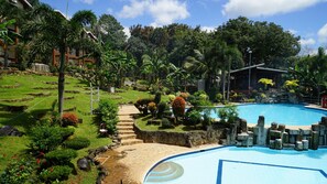 Ein Pool, der von einem angelegten Garten mit Steintreppen zum Pool umgeben ist, mit tropischer Vegetation und einem Gebäude im Hintergrund.