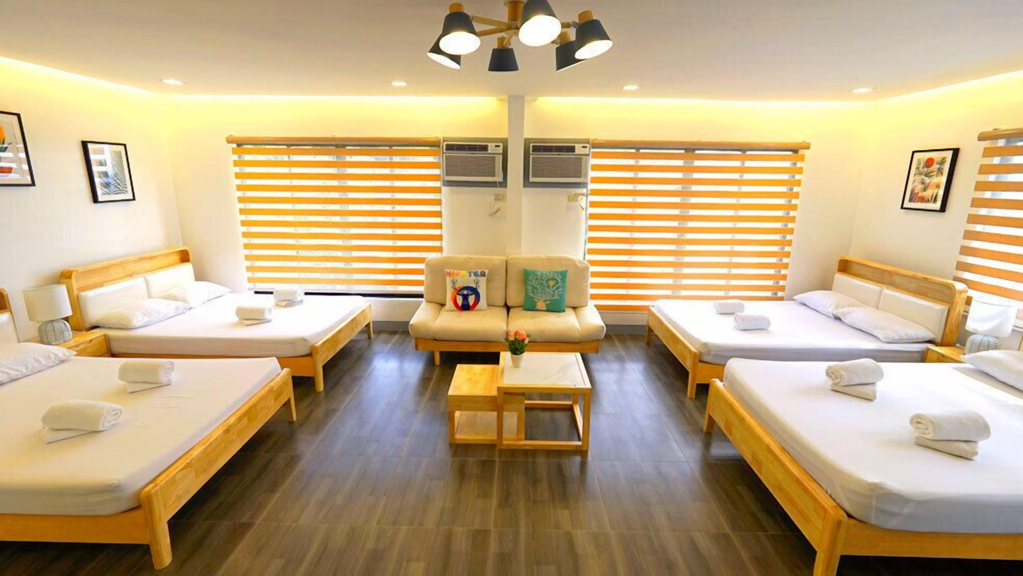 Habitación de hotel con cuatro camas individuales, un sofá y una mesita.