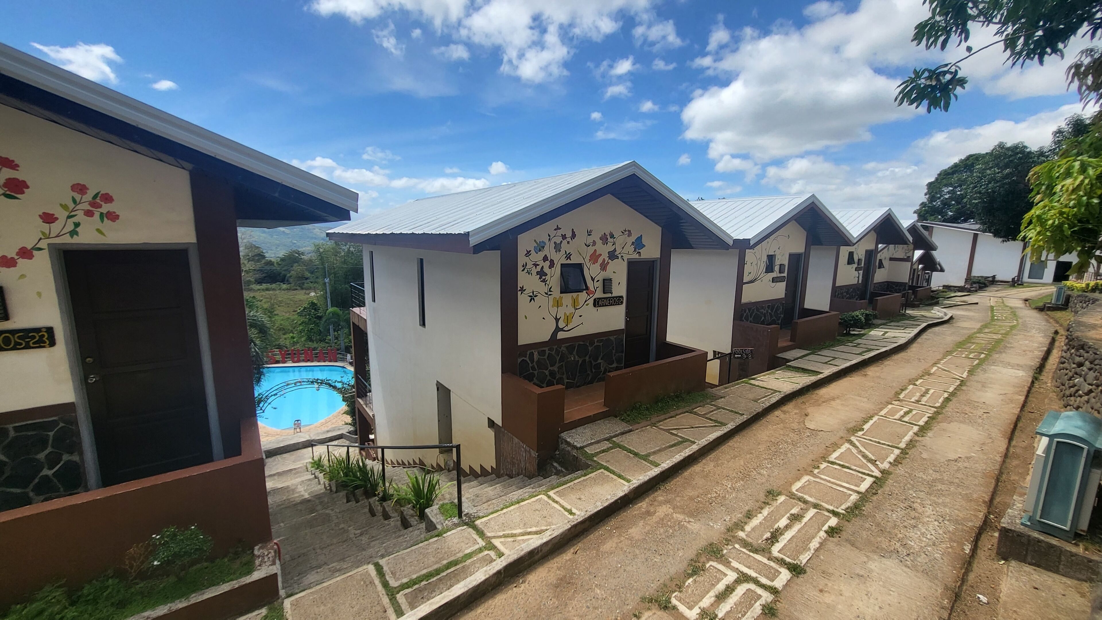 A row of small, single-story cabins with a swimming pool in the background.