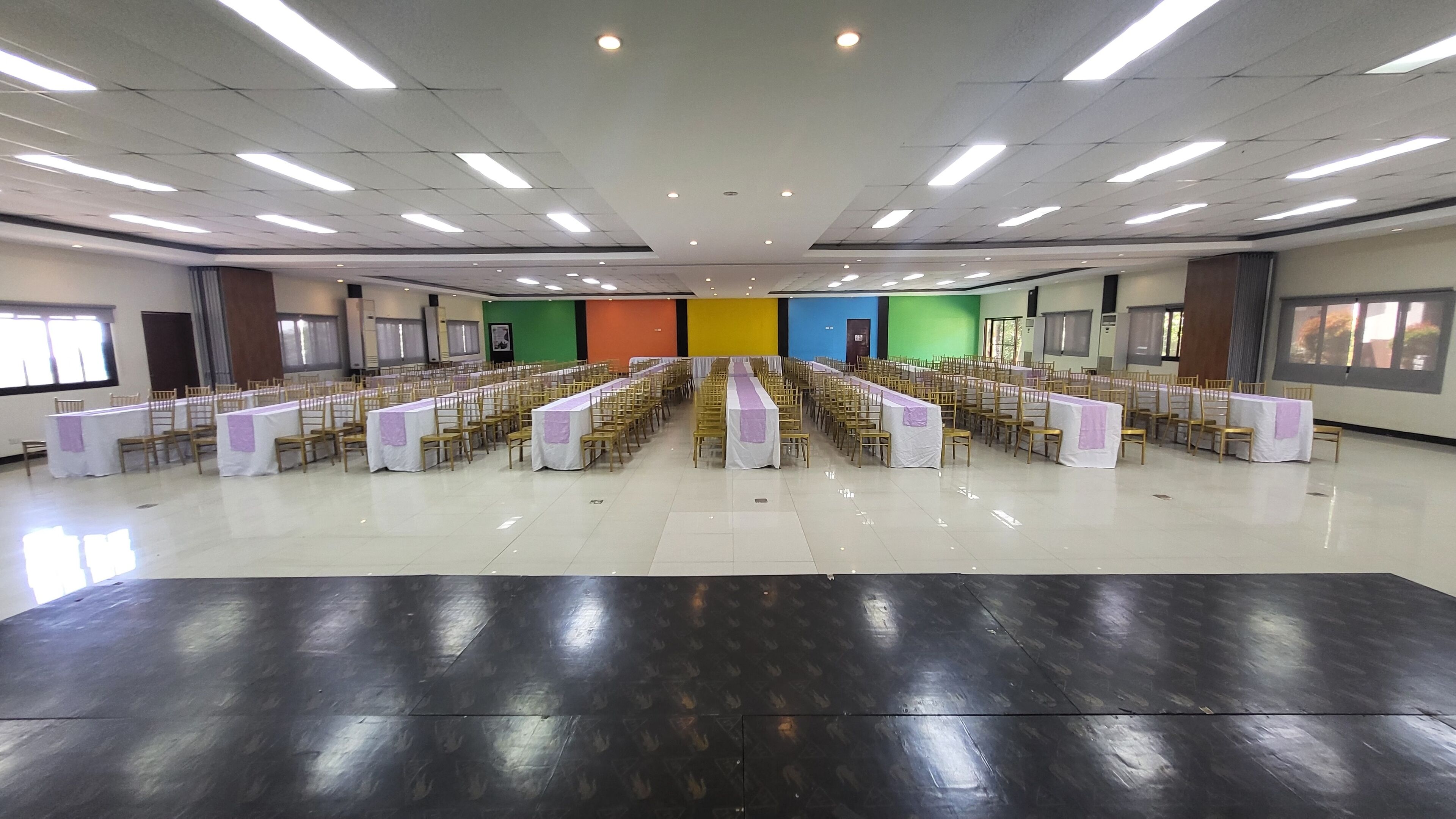 Un salón amplio con filas de mesas y sillas, un pasillo central y un techo alto con iluminación empotrada.