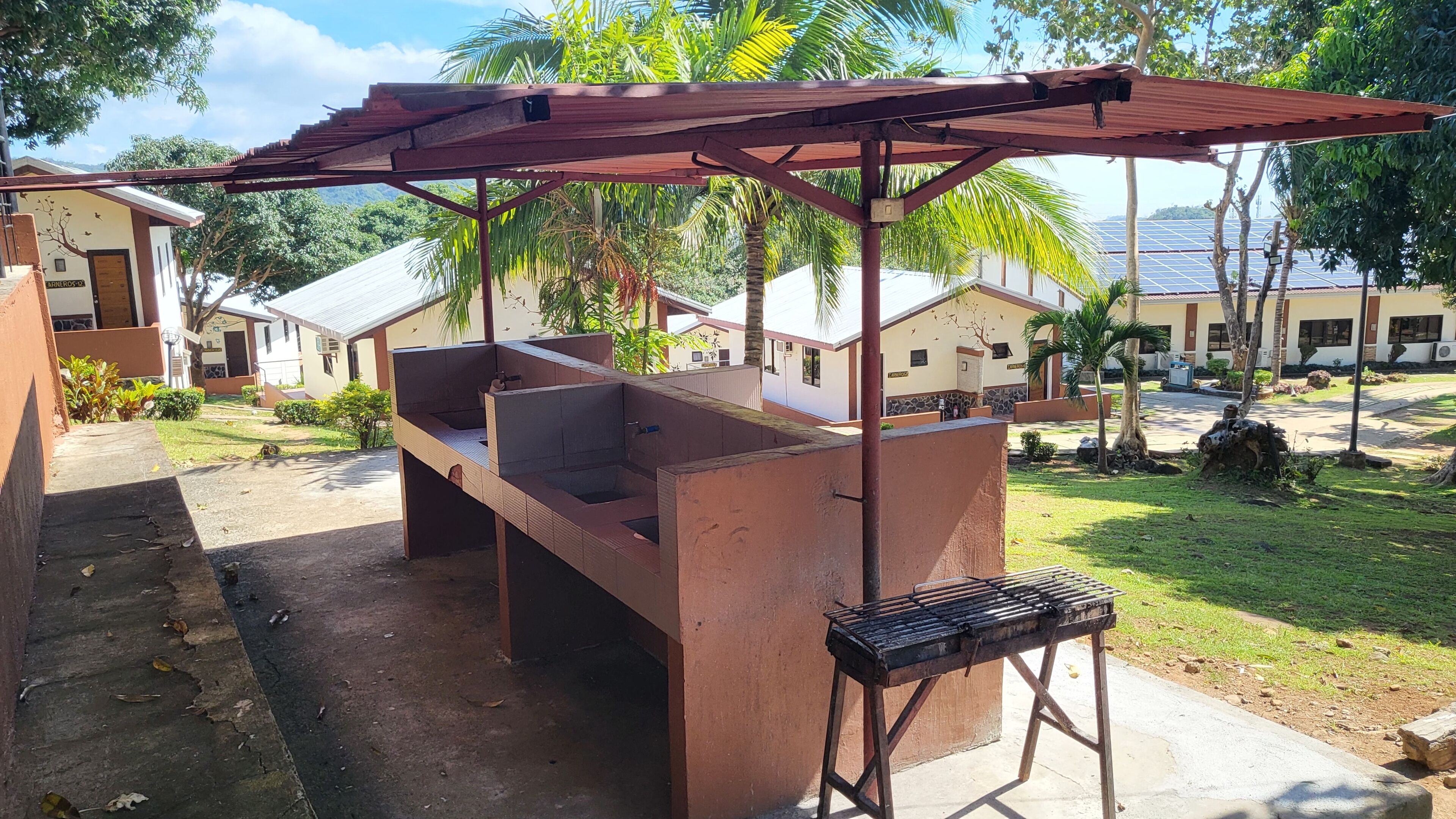 An outdoor barbecue area with a grill and seating under a wooden pergola.