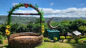 A rustic outdoor seating area with a woven basket, surrounded by greenery and a scenic view of hills. - Bakasyunan Resort Tanay (Tanay)