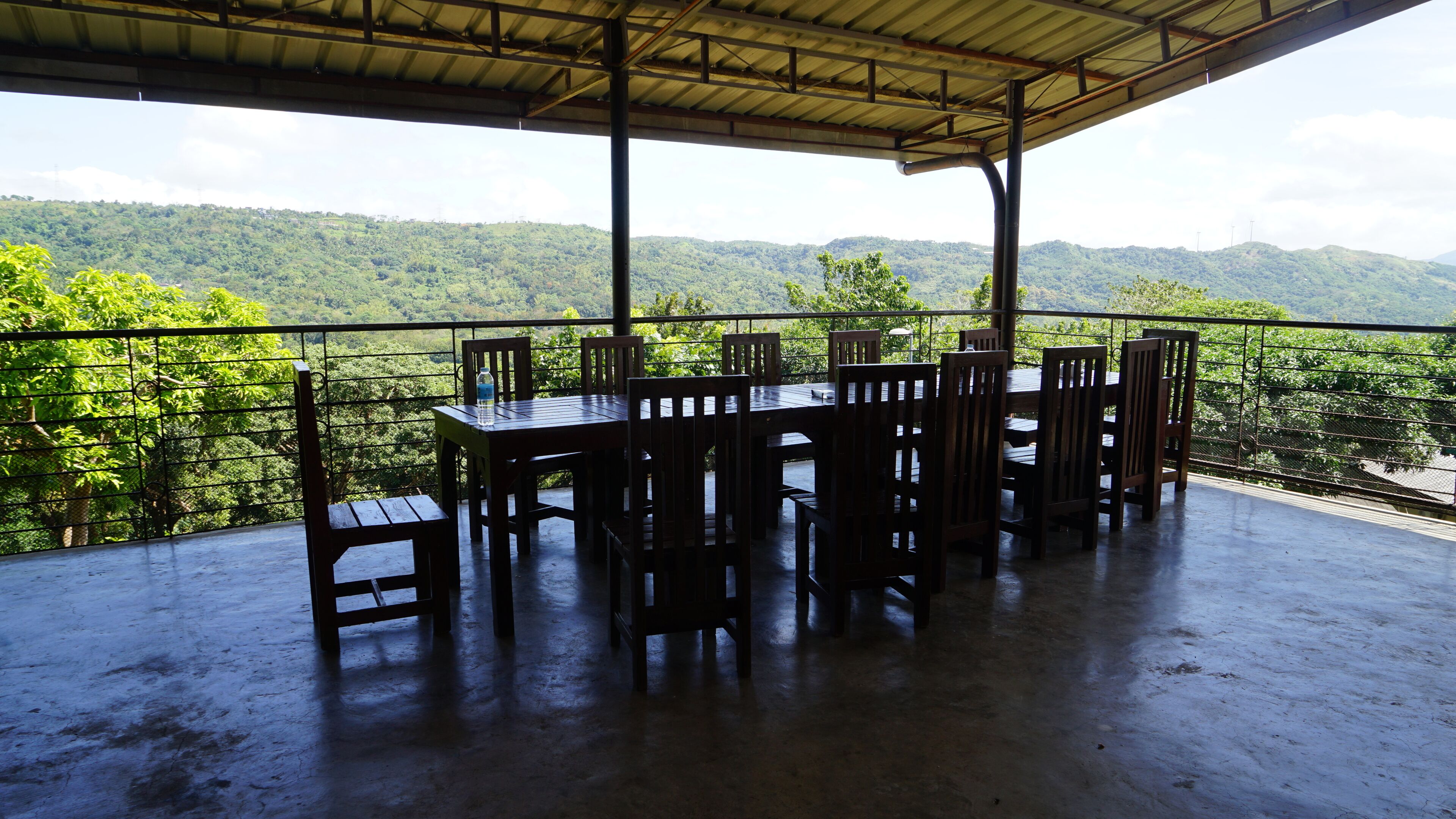 A covered outdoor seating area with a table and chairs, overlooking a lush green landscape.