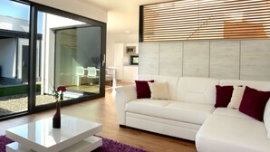 A modern living room with a white sofa, a coffee table, and a large window with blinds. - Apartmány Eden (Luhacovice)