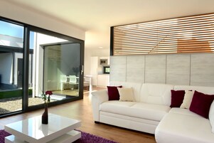 Una sala de estar moderna con un sofá blanco, una mesa de centro y un ventanal con persianas.