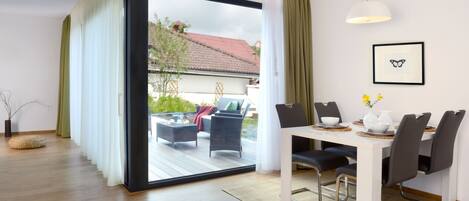 A modern dining area with a sliding glass door leading to an outdoor patio, a dining table with chairs, and a pendant light.