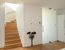 Un interior moderno con una escalera de madera, una puerta blanca y un jarrón con flores.