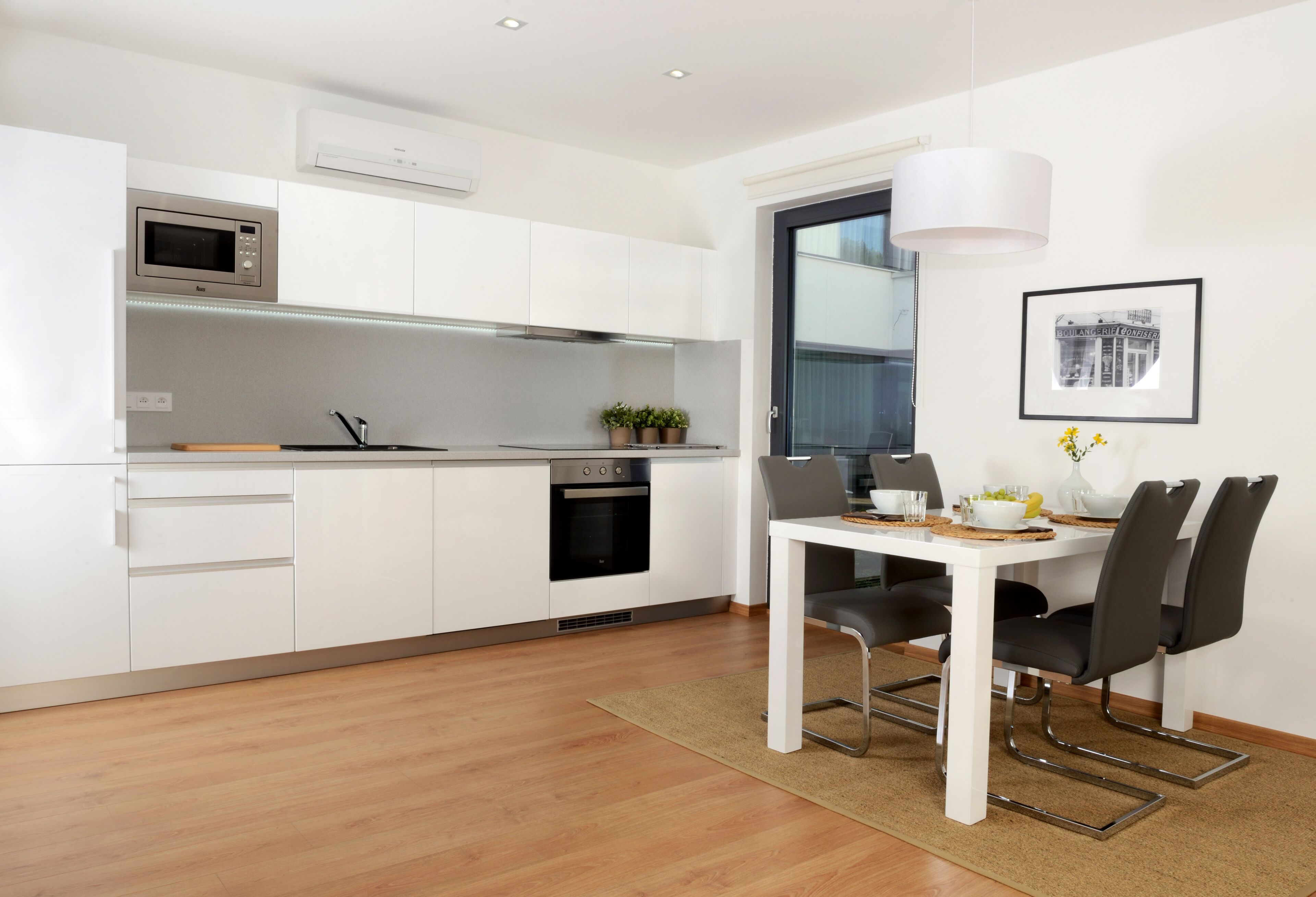 A modern kitchen with white cabinets, a microwave, an oven, and a dining area with a table and chairs.