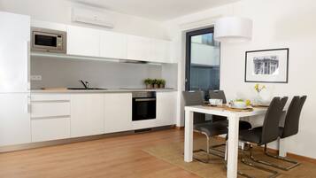 A modern kitchen with white cabinets, a microwave, an oven, and a dining area with a table and chairs.