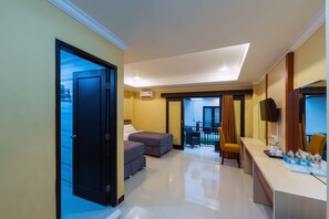A hotel room with a large bed, a sitting area with a chair, a small table with a mirror, and a balcony with a view. - Sylvia Bali Suite Residence (Denpasar)