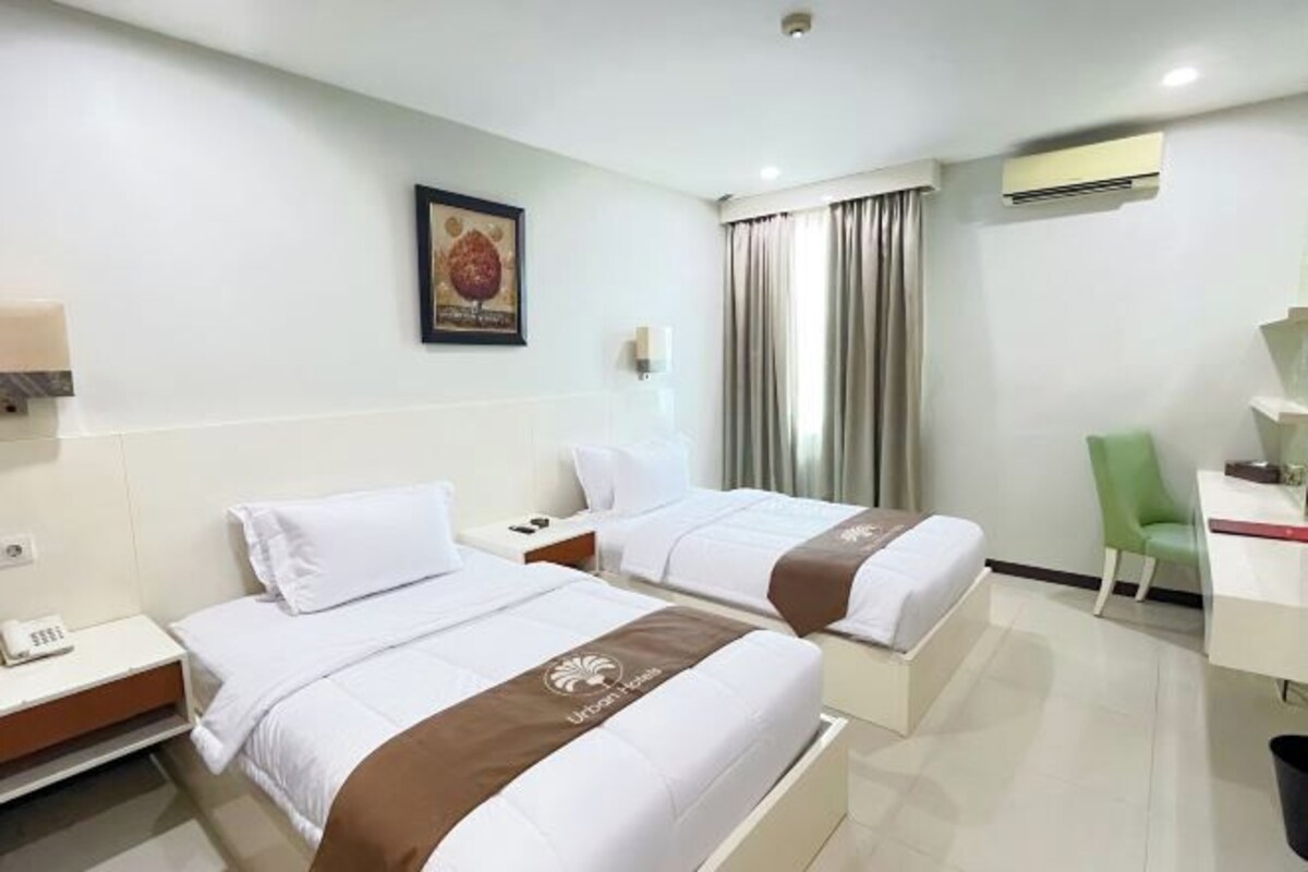 A hotel room with two beds, a desk, a chair, and a window with curtains.