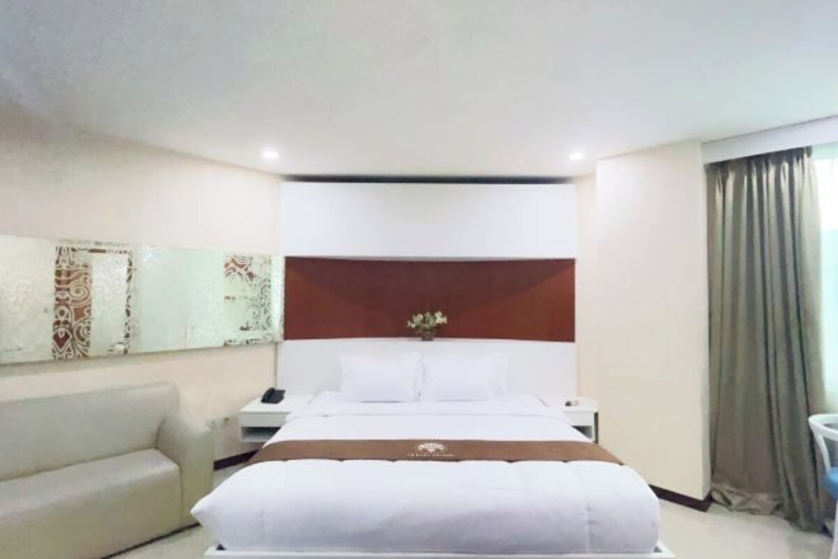 A hotel room with a large bed, a bedside table, a nightstand, a sofa, and a decorative wall piece.