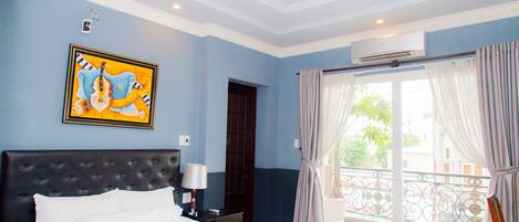 A hotel room with a large bed, a painting on the wall, an air conditioning unit, and a balcony with curtains.