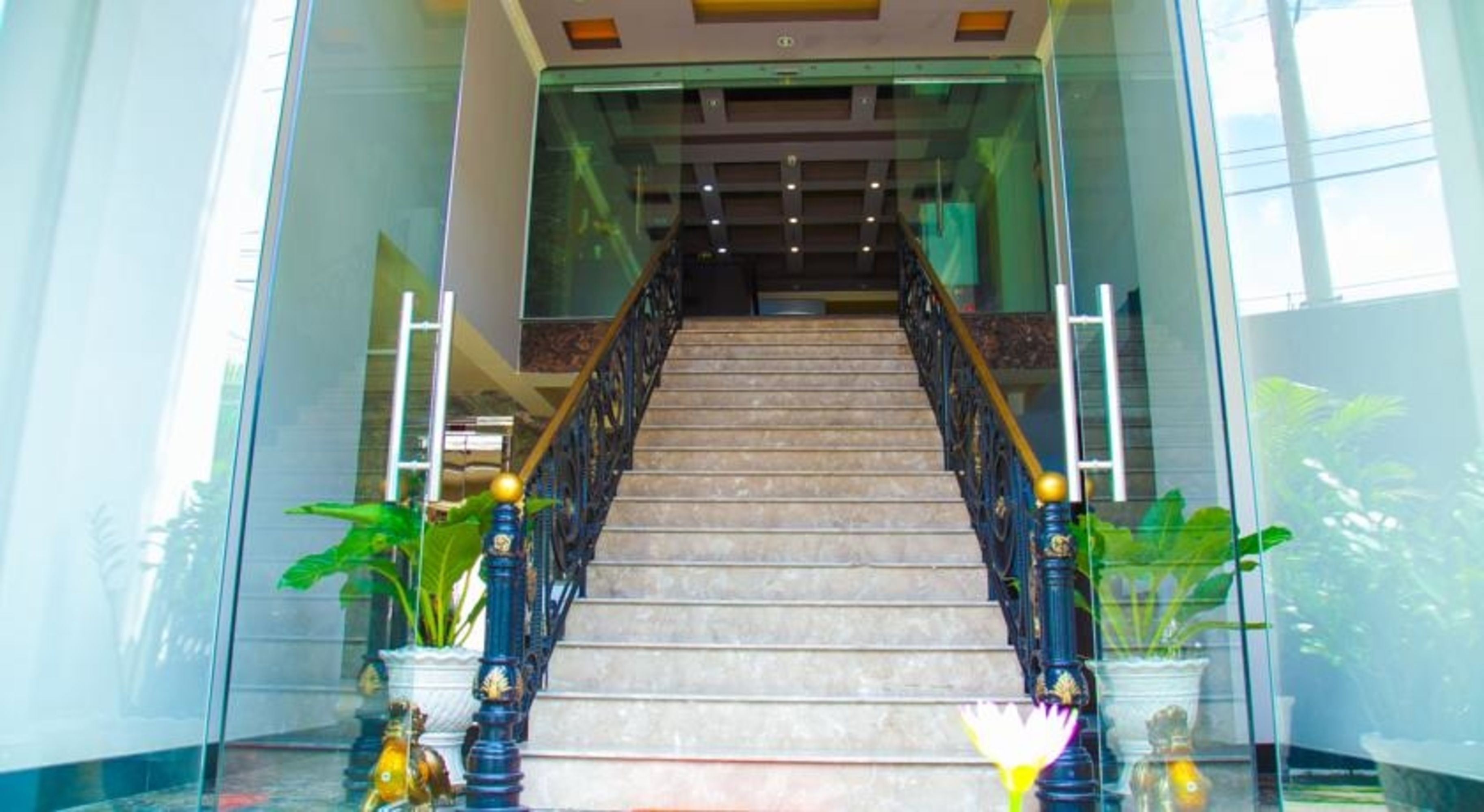Una escalera de mármol con barandillas negras y esferas doradas, que conduce a una puerta de entrada de vidrio.