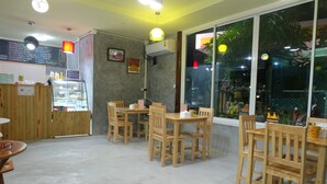 A cafe with wooden furniture, a glass display case, and a menu board. - Samui Poshtel (Koh Samui)
