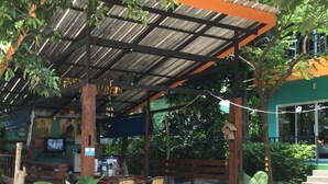 An outdoor seating area with a wooden pergola, tables, chairs, and potted plants. - Samui Poshtel (Koh Samui)
