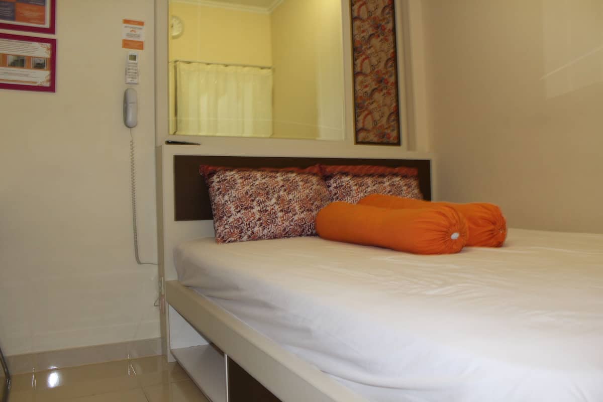 A single bed with an orange pillow, a patterned pillow, and a white bedspread.