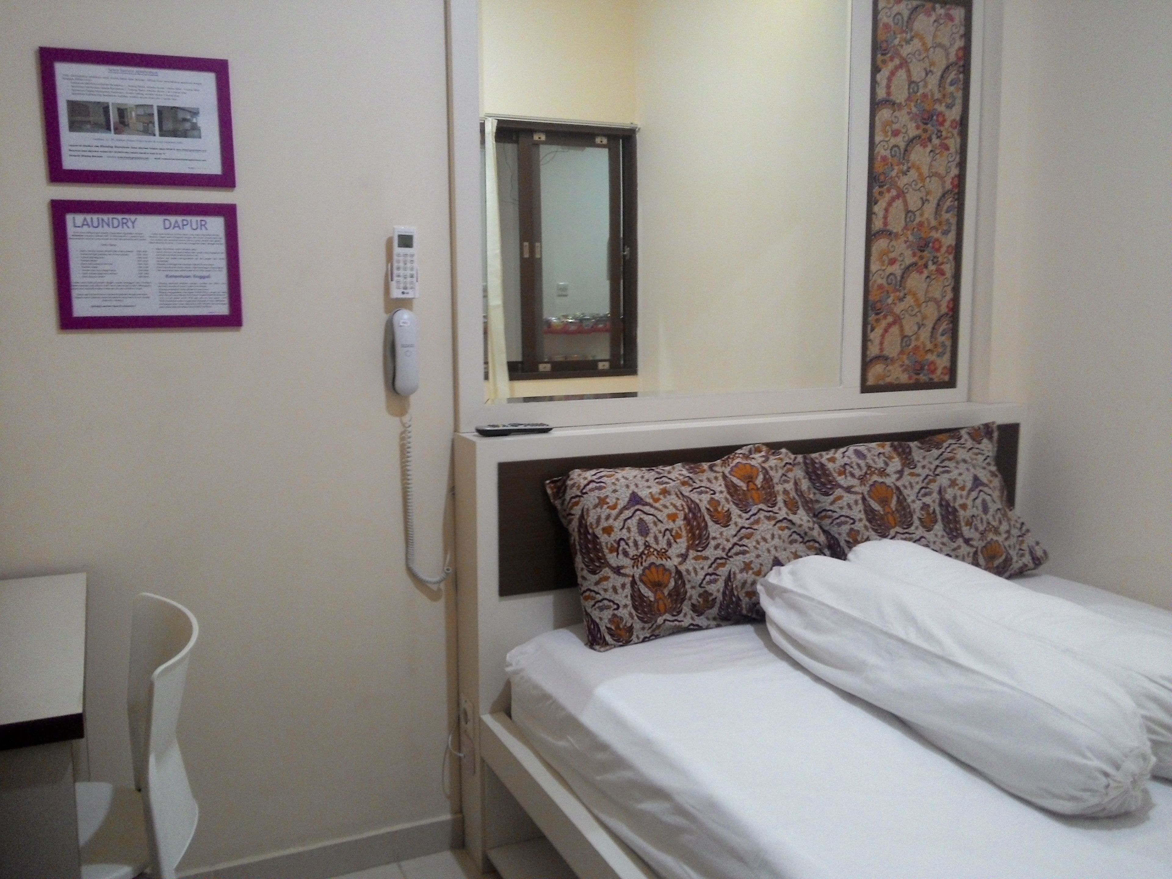 A hotel room with a bed, a bedside table, a telephone, and two informational posters on the wall.
