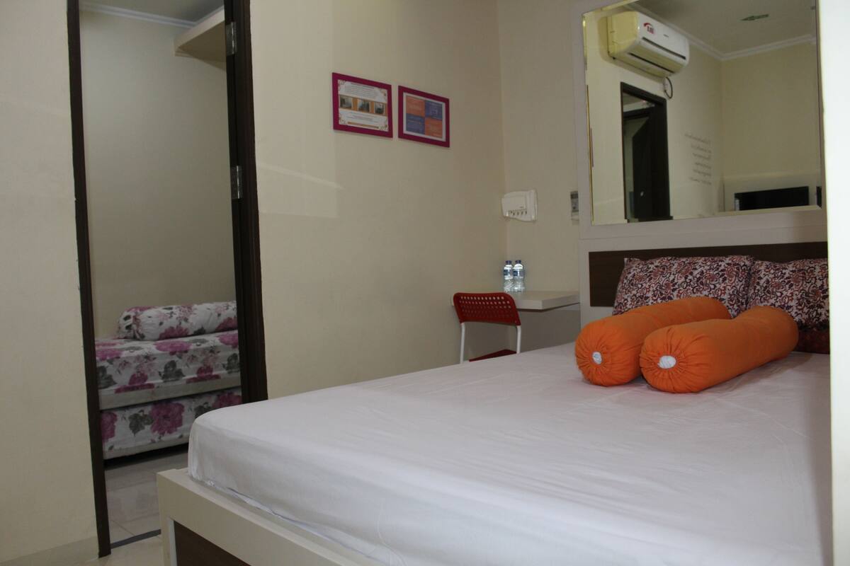 A hotel room with a bed, a small desk, a chair, a water bottle, and a mirror on the wall.