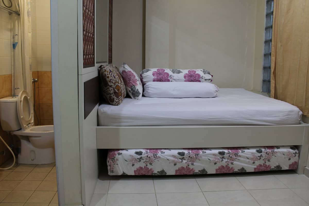 A small, single-bed room with a shower area and a toilet.