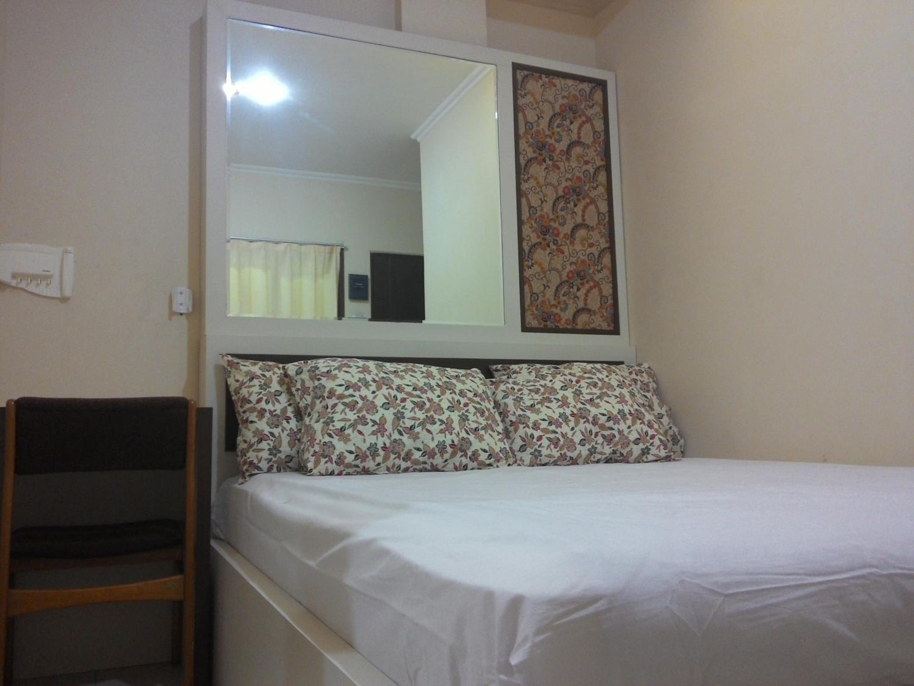 A bedroom with a bed, a wooden chair, a mirror, and a decorative wall piece.