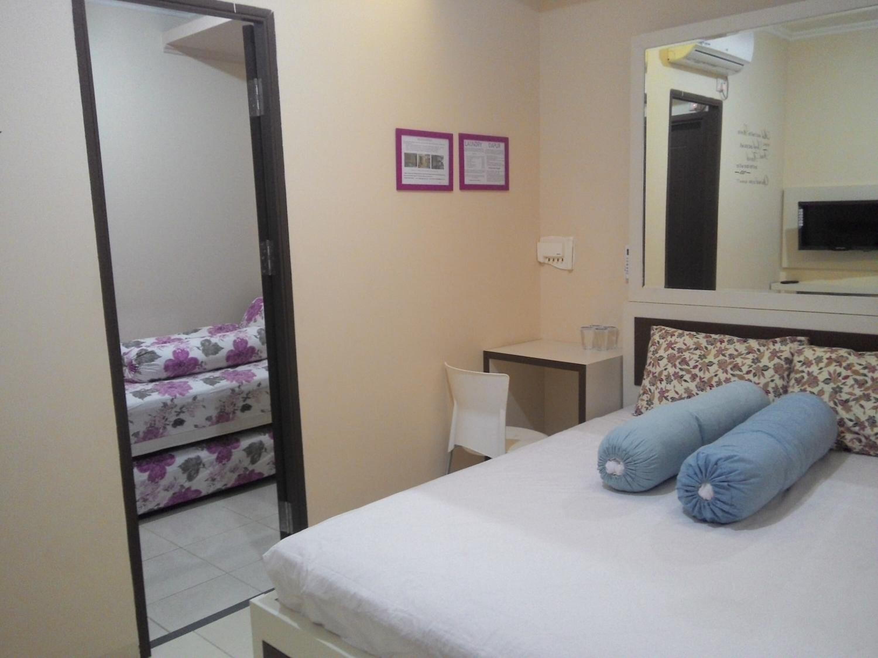 A bedroom with a bed, a desk, a chair, and a mirror.