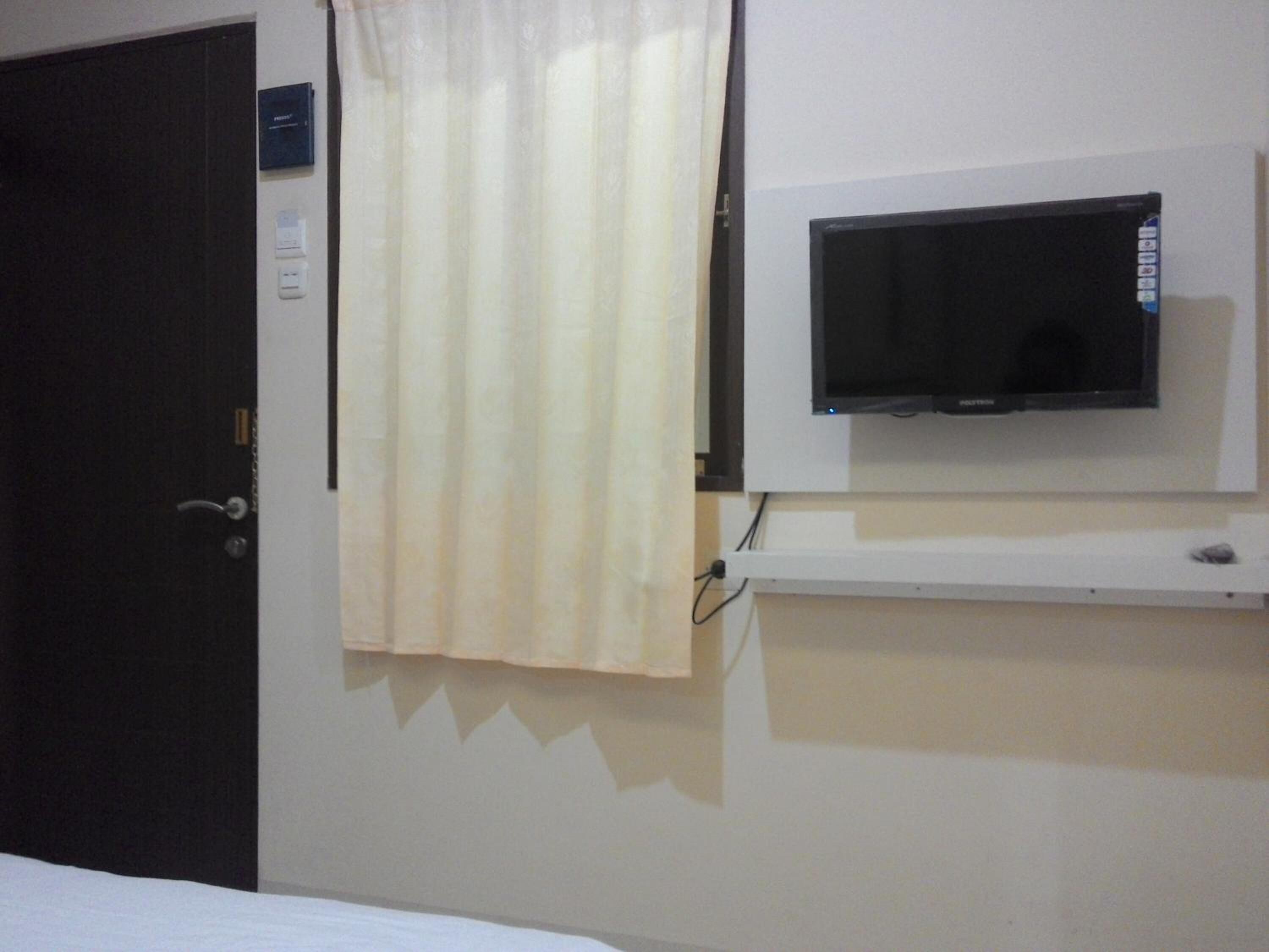 A hotel room with a closed door, a television mounted on the wall, and a curtain partially drawn.