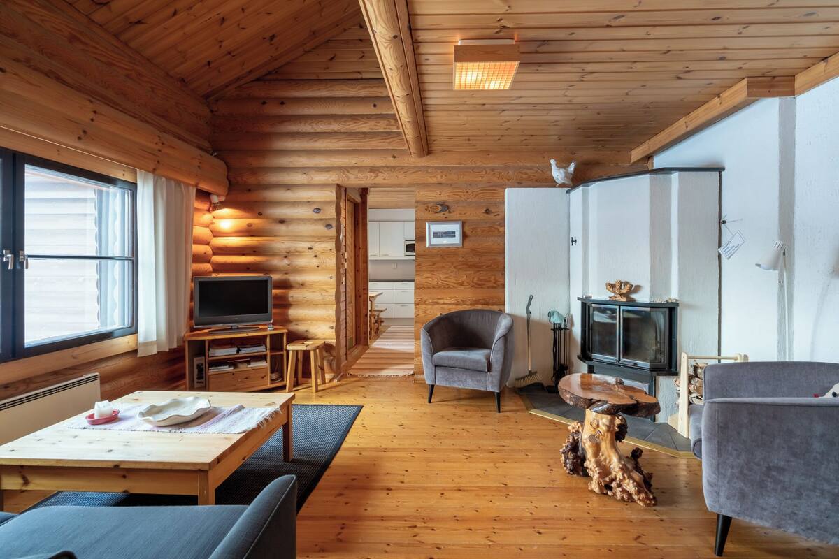 Un accogliente interno di una baita con pavimento in legno, una televisione, un camino e un'area pranzo.