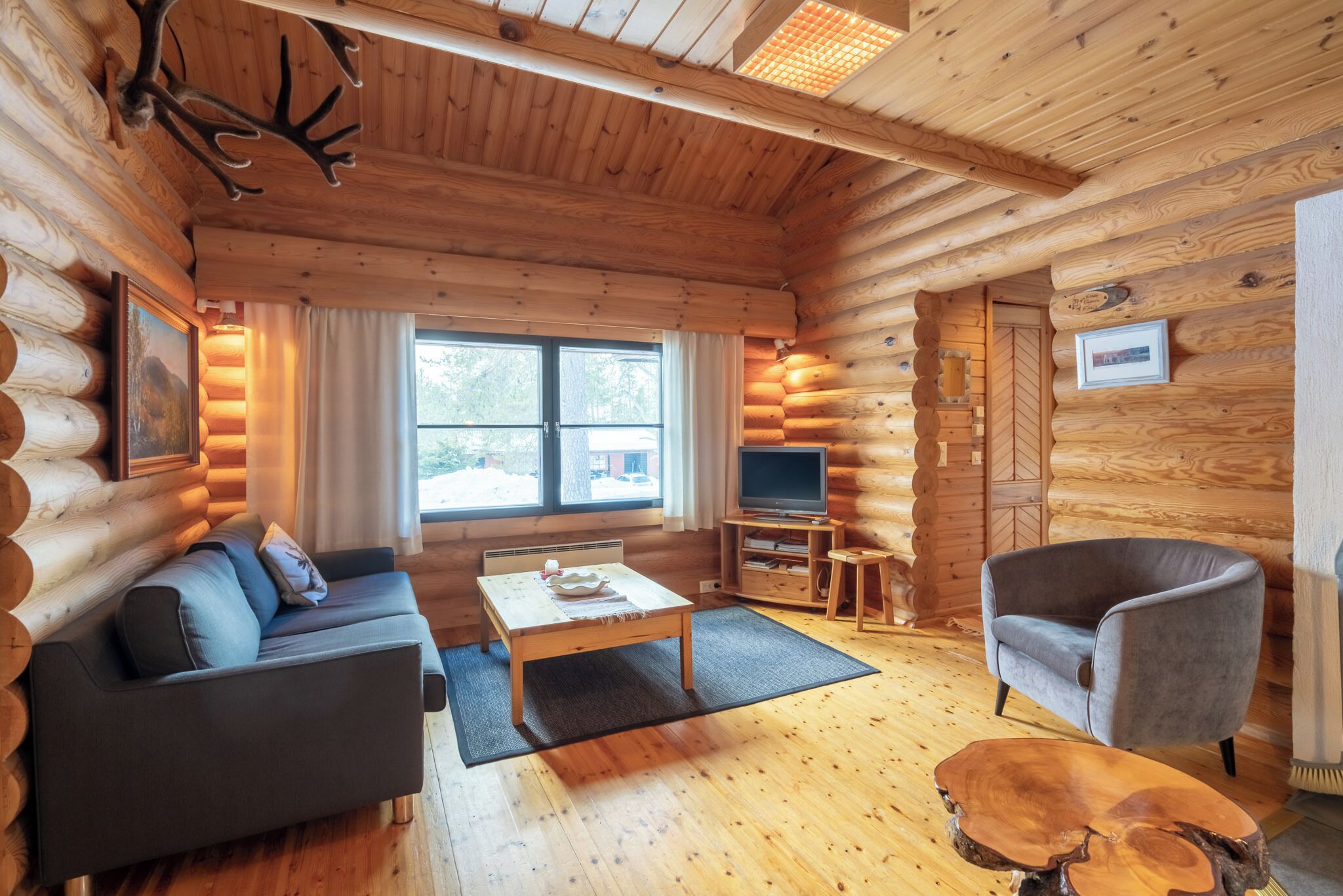 A log cabin interior with a sofa, a coffee table, a TV stand, and a chair.