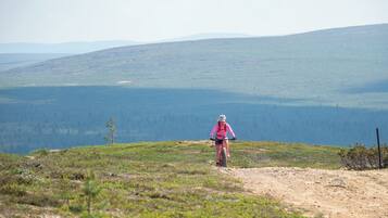 Une personne fait du vélo tout terrain sur un sentier de terre, avec une vue panoramique sur un lac et des collines en arrière-plan.