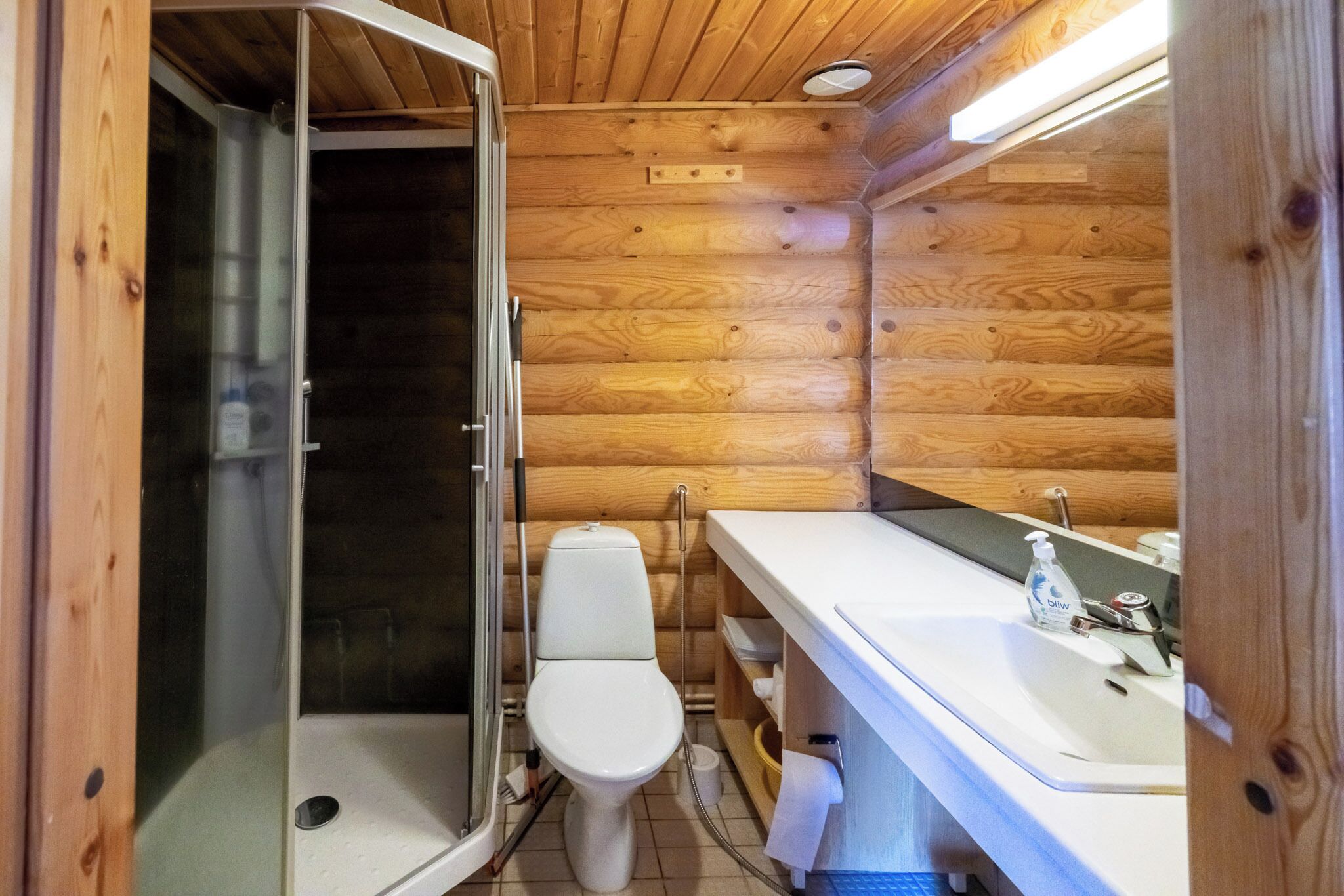 A wooden cabin bathroom with a shower, toilet, and sink.