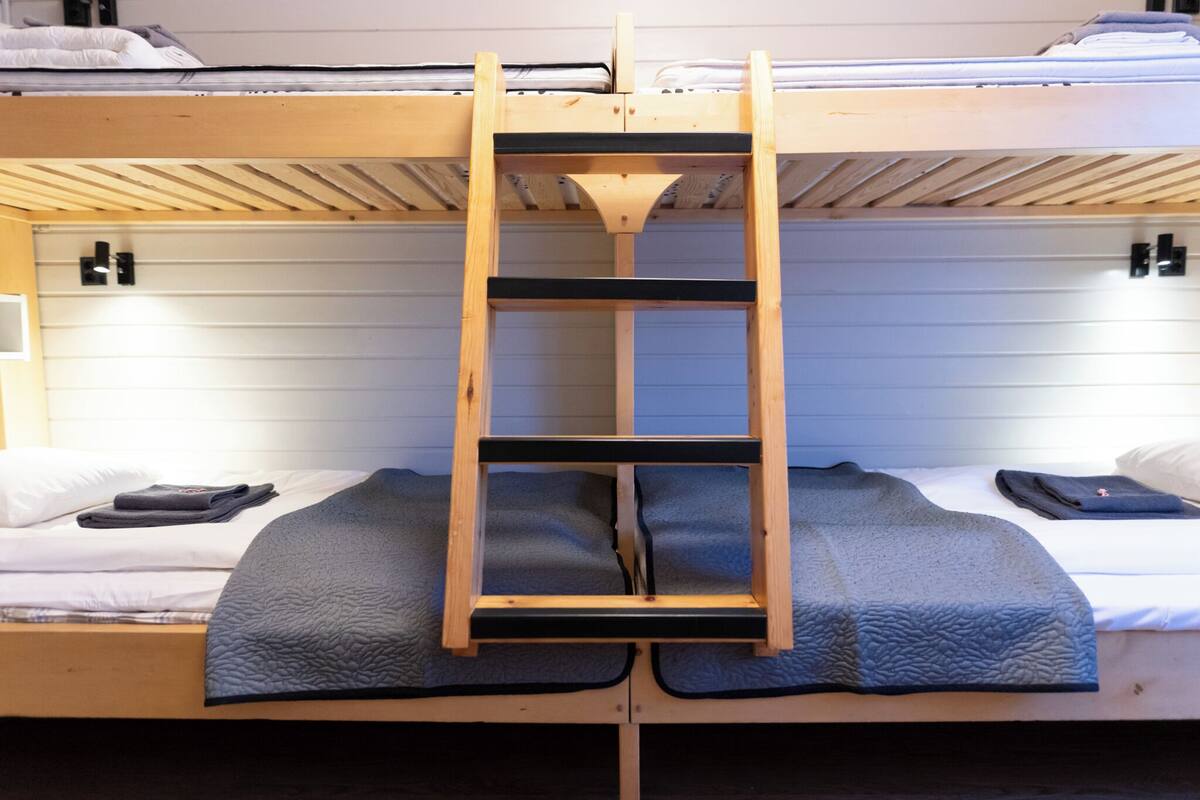 Un letto a castello con una scala in legno, due cuscini e una coperta piegata su ogni letto.