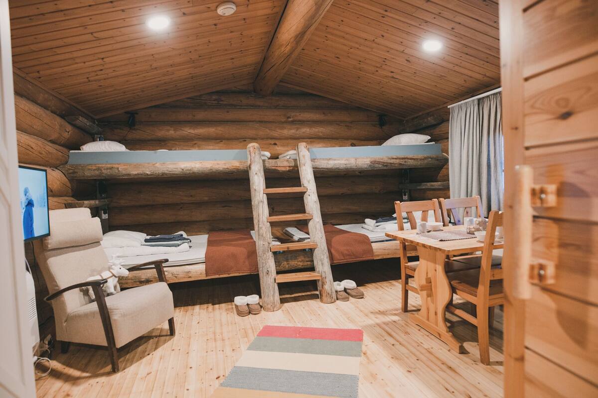 Accogliente camera in una baita di legno con un letto a castello, una scala in legno, una scrivania con sedie e un televisore.