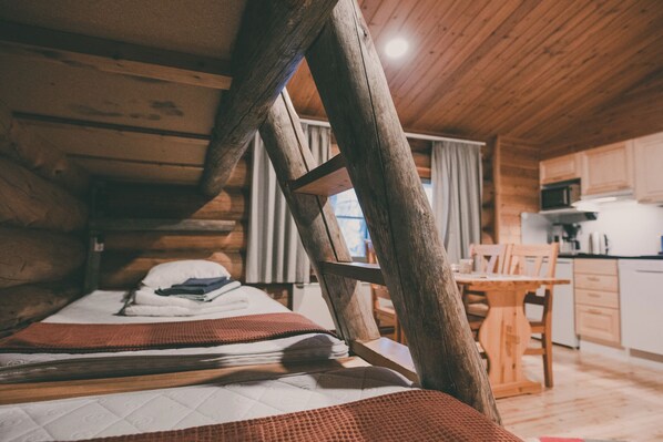 Acogedora habitación de estilo cabaña con techo de madera, cama con colcha, mesa de madera y una zona de cocina con armarios y microondas.