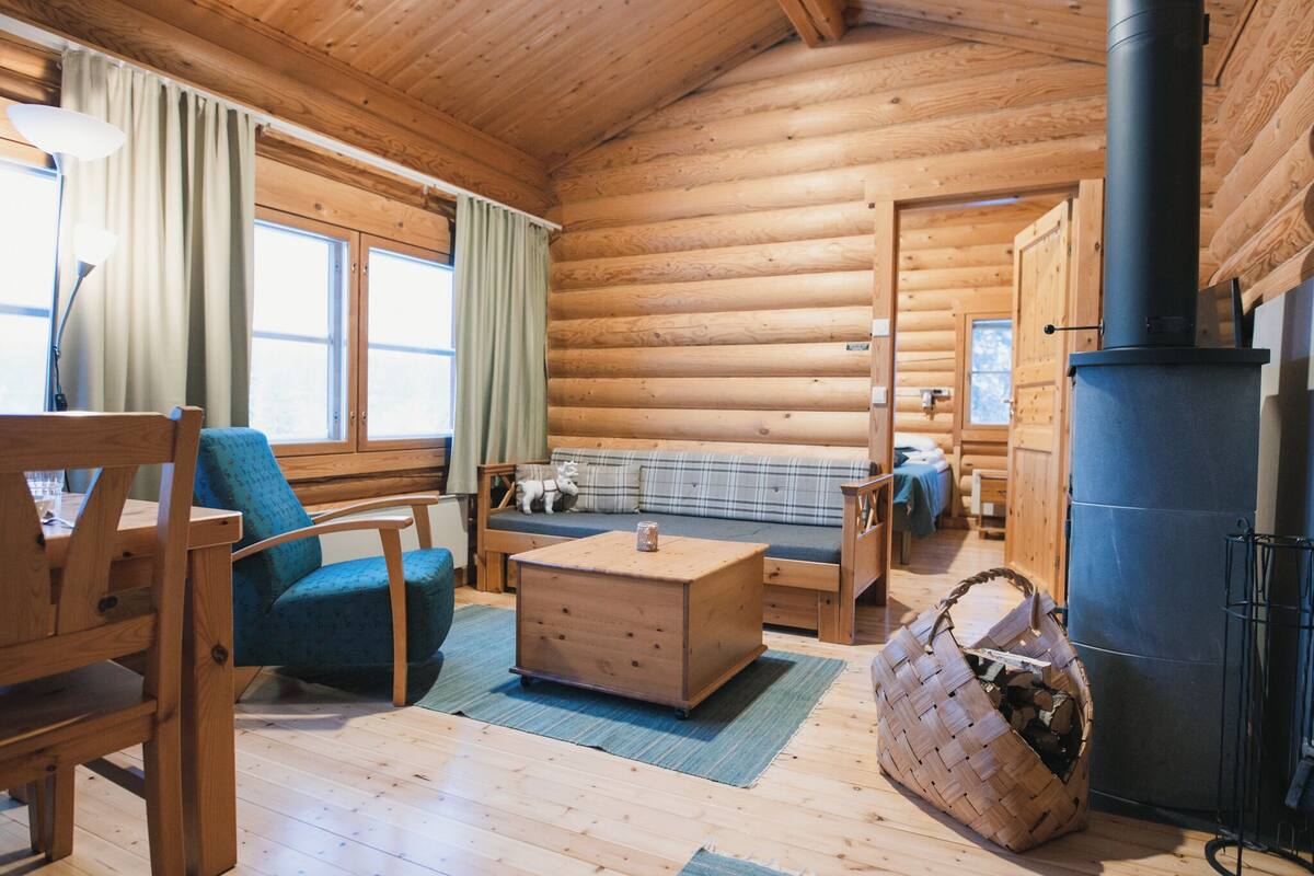 Interno di una baita con un divano in legno, un tavolo di legno, una poltrona blu e un camino.