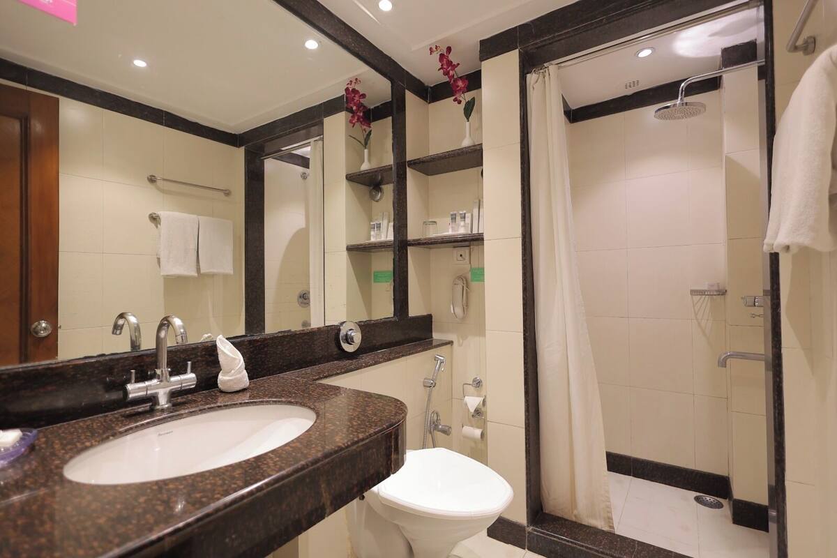 A bathroom with a sink, mirror, toilet, shower, and a towel rack.