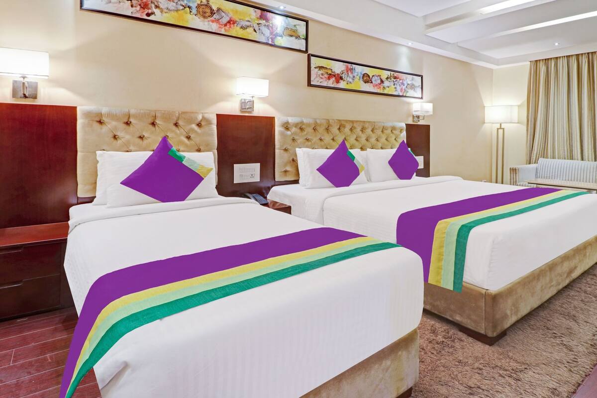 Quarto de hotel com duas camas, um sofá e obras de arte nas paredes.