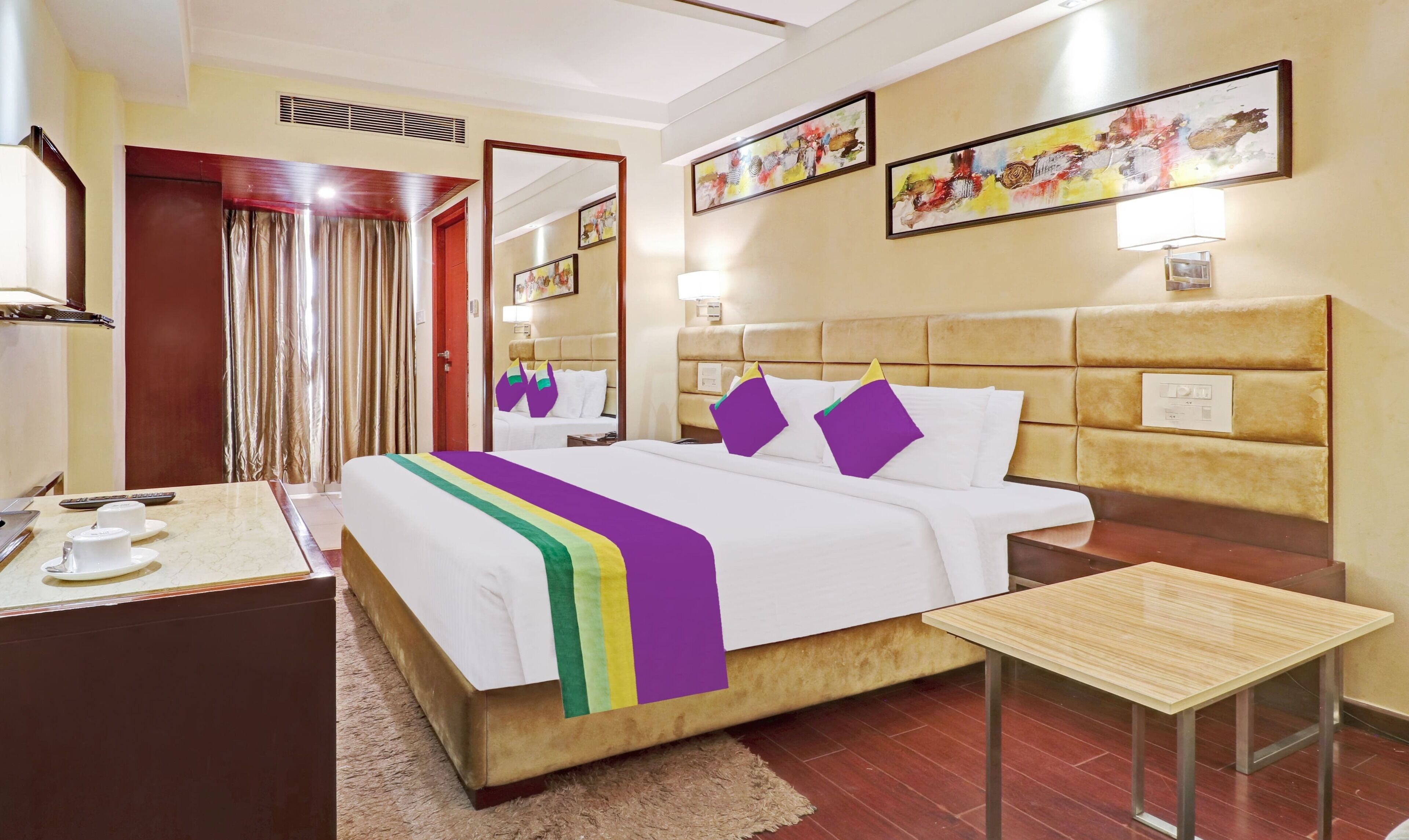 Een hotelkamer met een bed, nachtkastje en een klein bureau met een lamp.